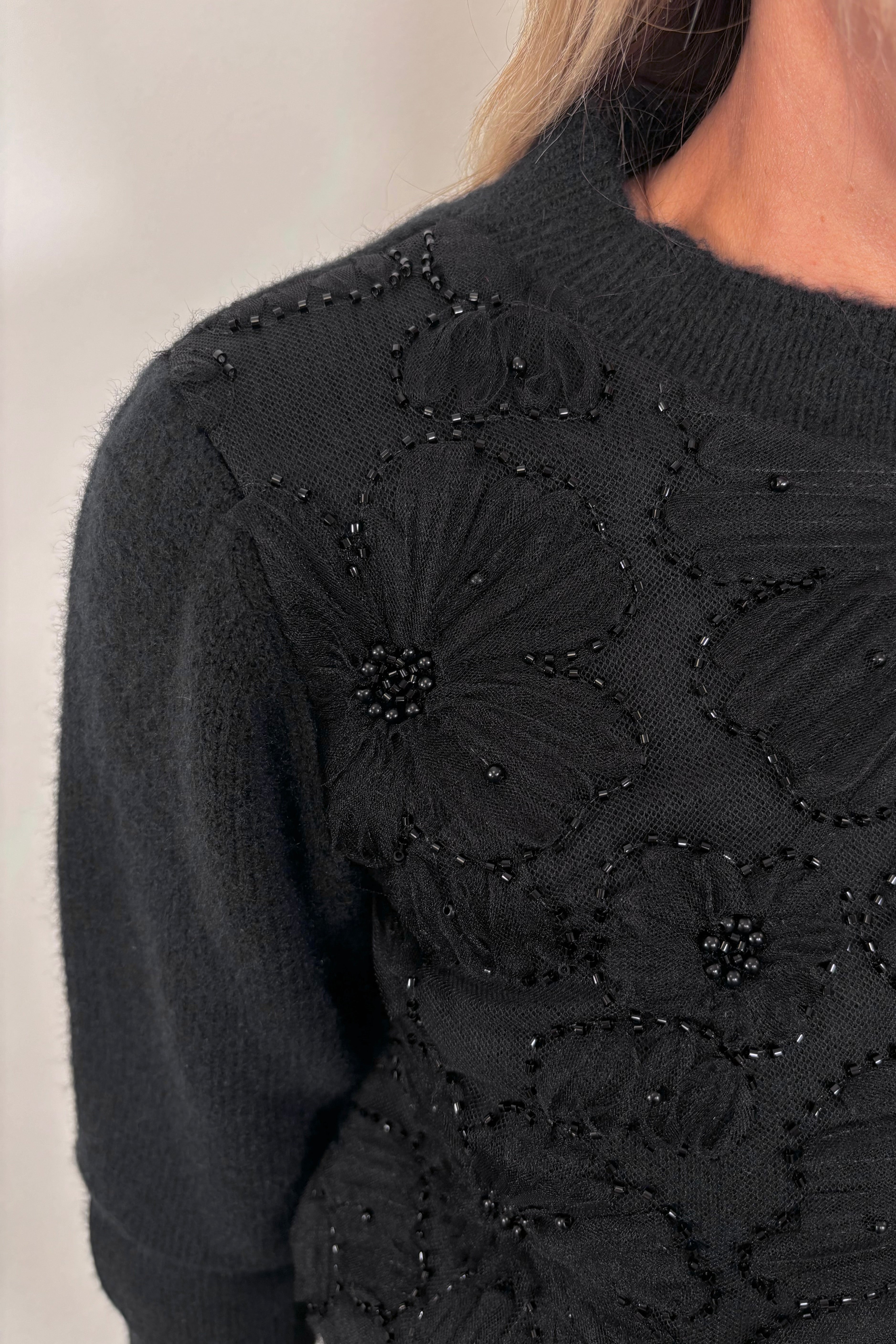 Close up of woman wearing a floral detailed sweater with pearls