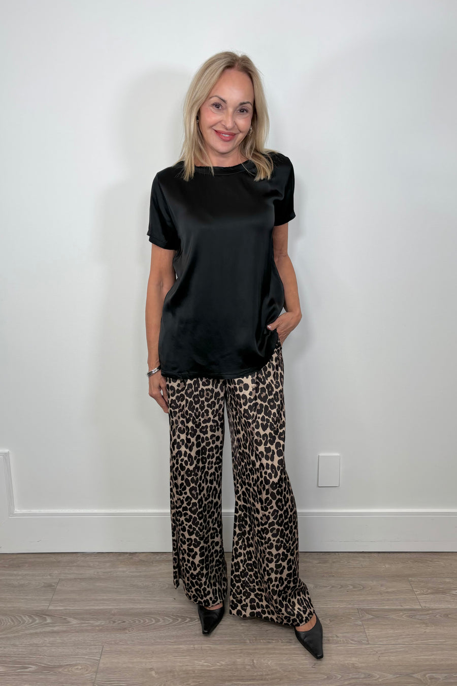 Front view of woman wearing a satin black shirt paired with leopard print satin pants