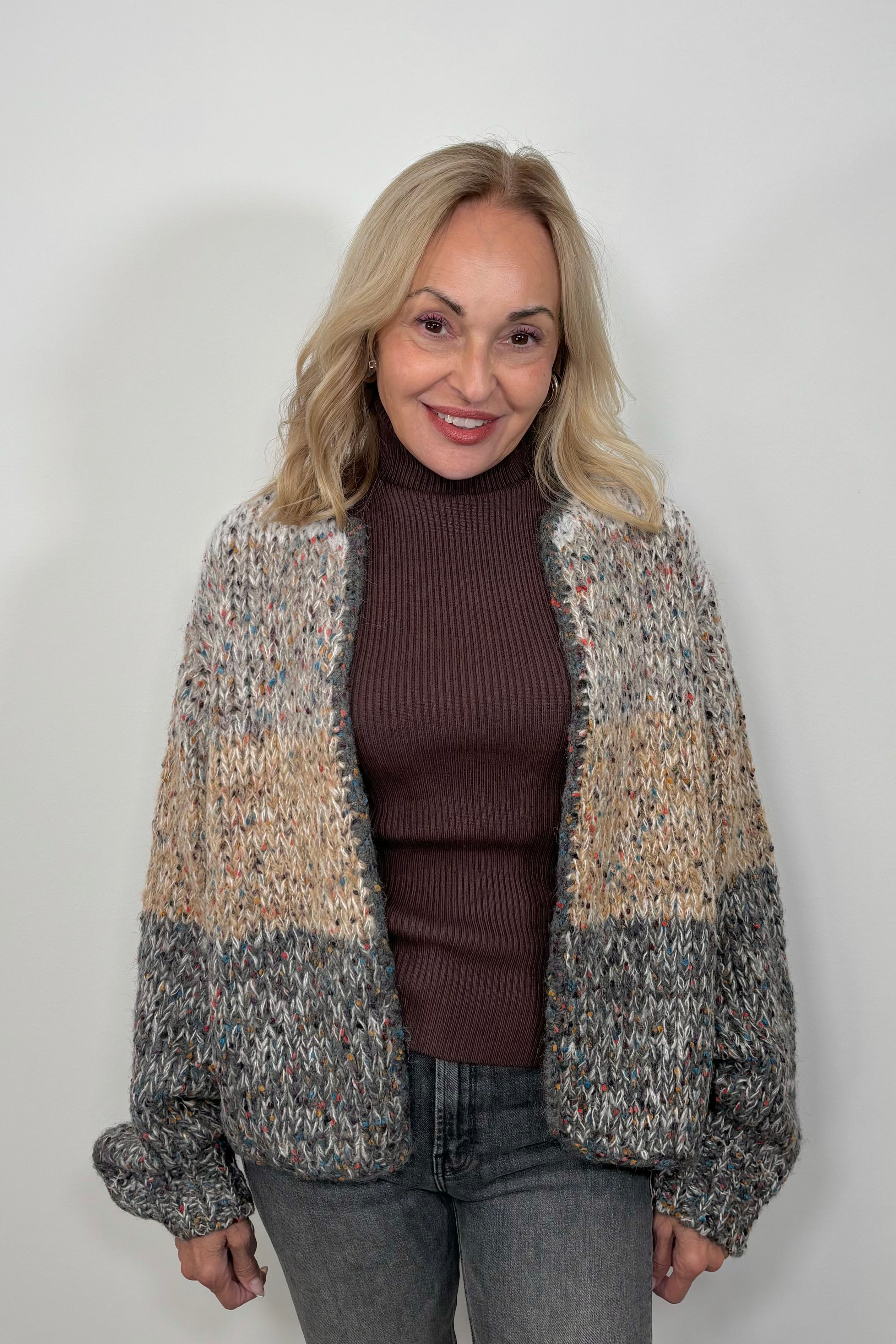 Front view of woman wearing a light gray, beige and dark gray knitted cardigan