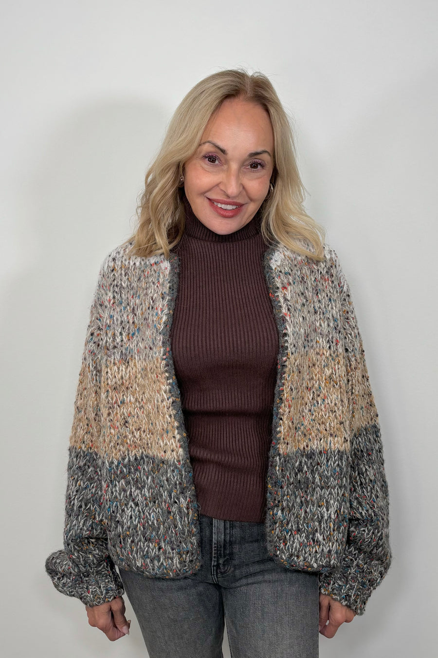 Front view of woman wearing a light gray, beige and dark gray knitted cardigan