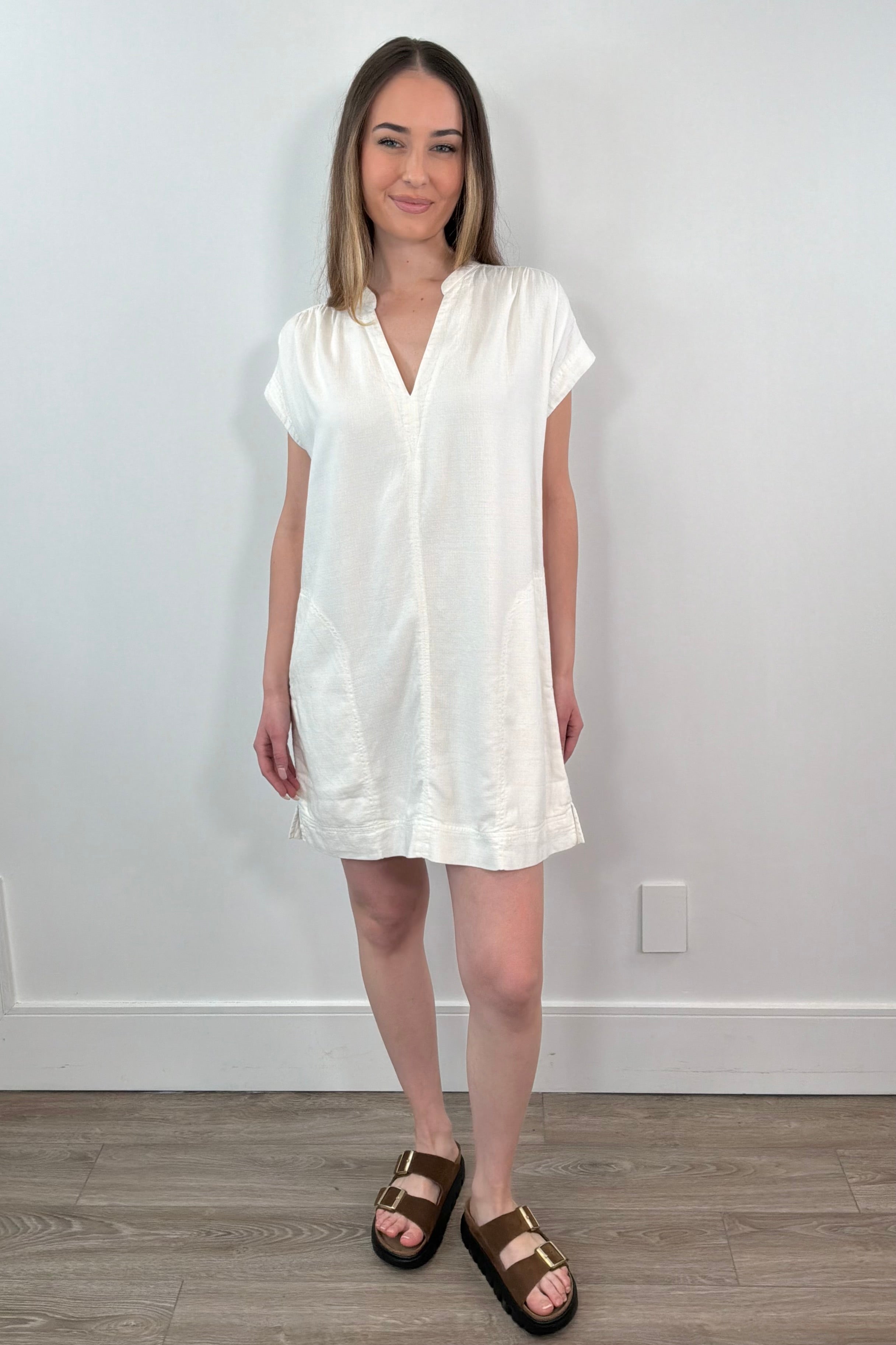 Woman wearing a white dress standing against a plain white wall.