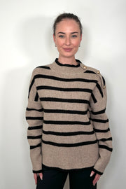 Front view of a woman wearing a walnut coloured sweater with stripes and buttons on the left shoulder