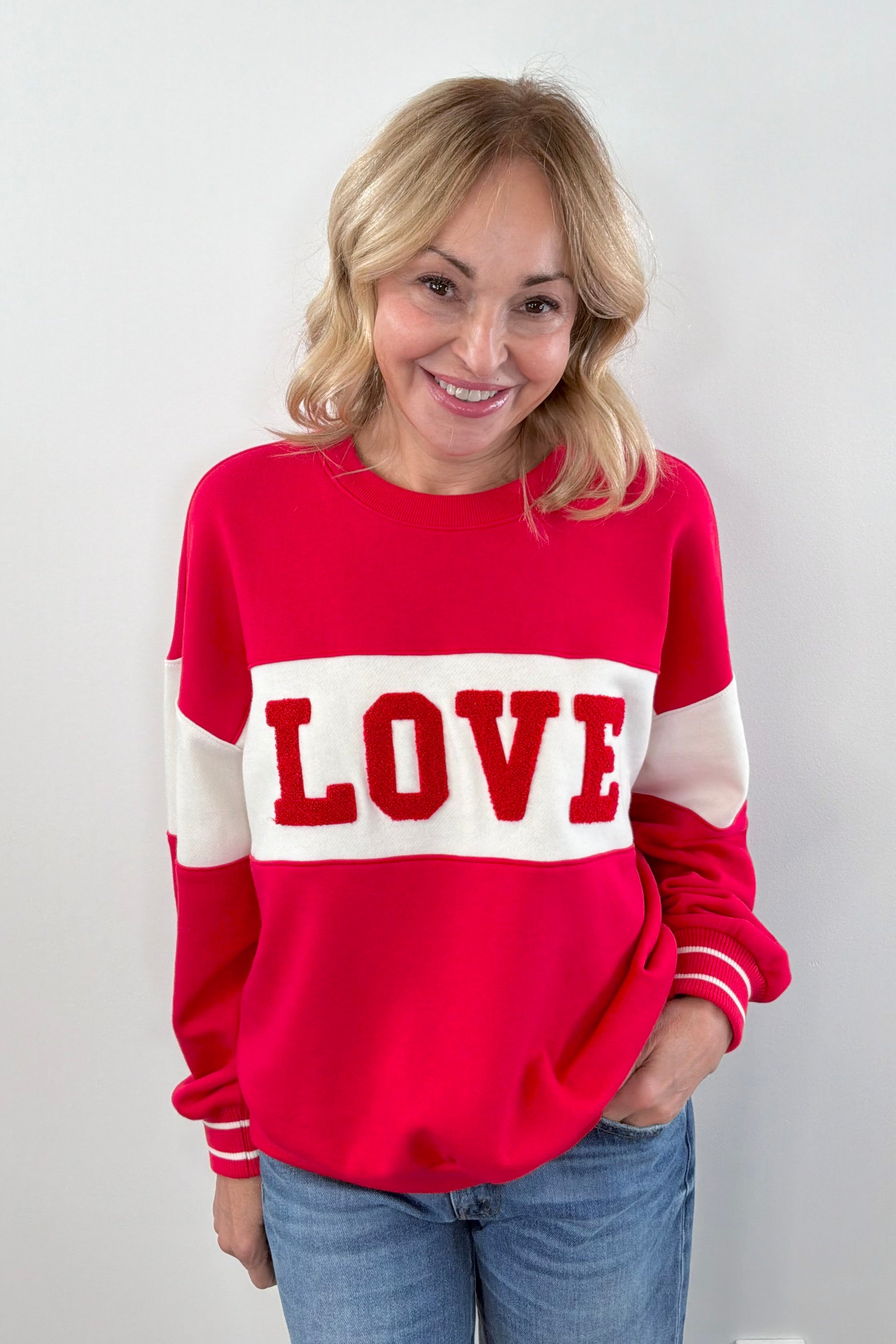 Woman wearing wearing a red and off white color block crewneck sweatshirt with the word "LOVE" written in chenille