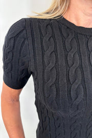 Close up view of woman wearing a black coloured cable knit top