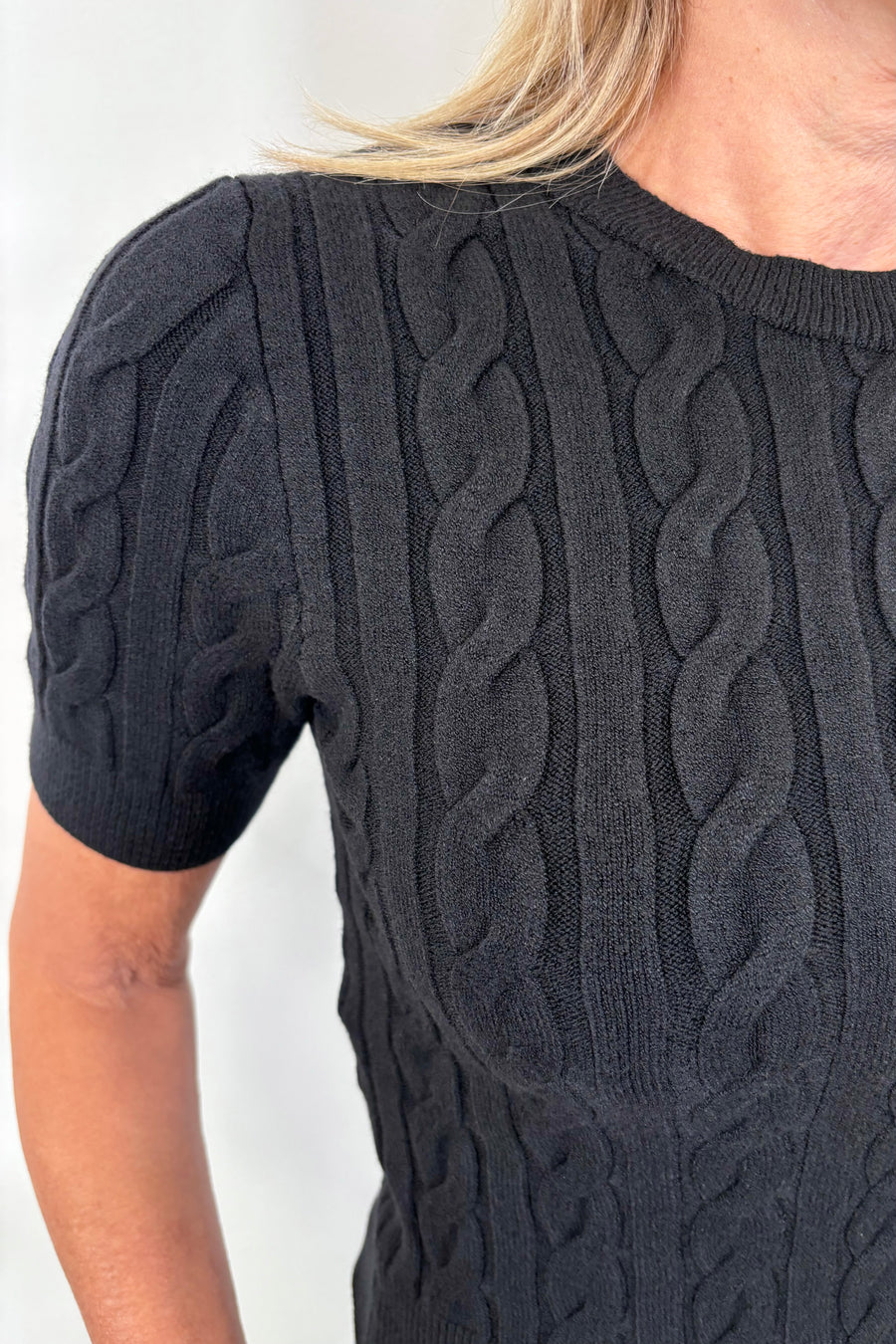 Close up view of woman wearing a black coloured cable knit top