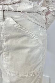 Close up view of a person wearing oat-coloured corduroy pants and white sneakers on a plain background