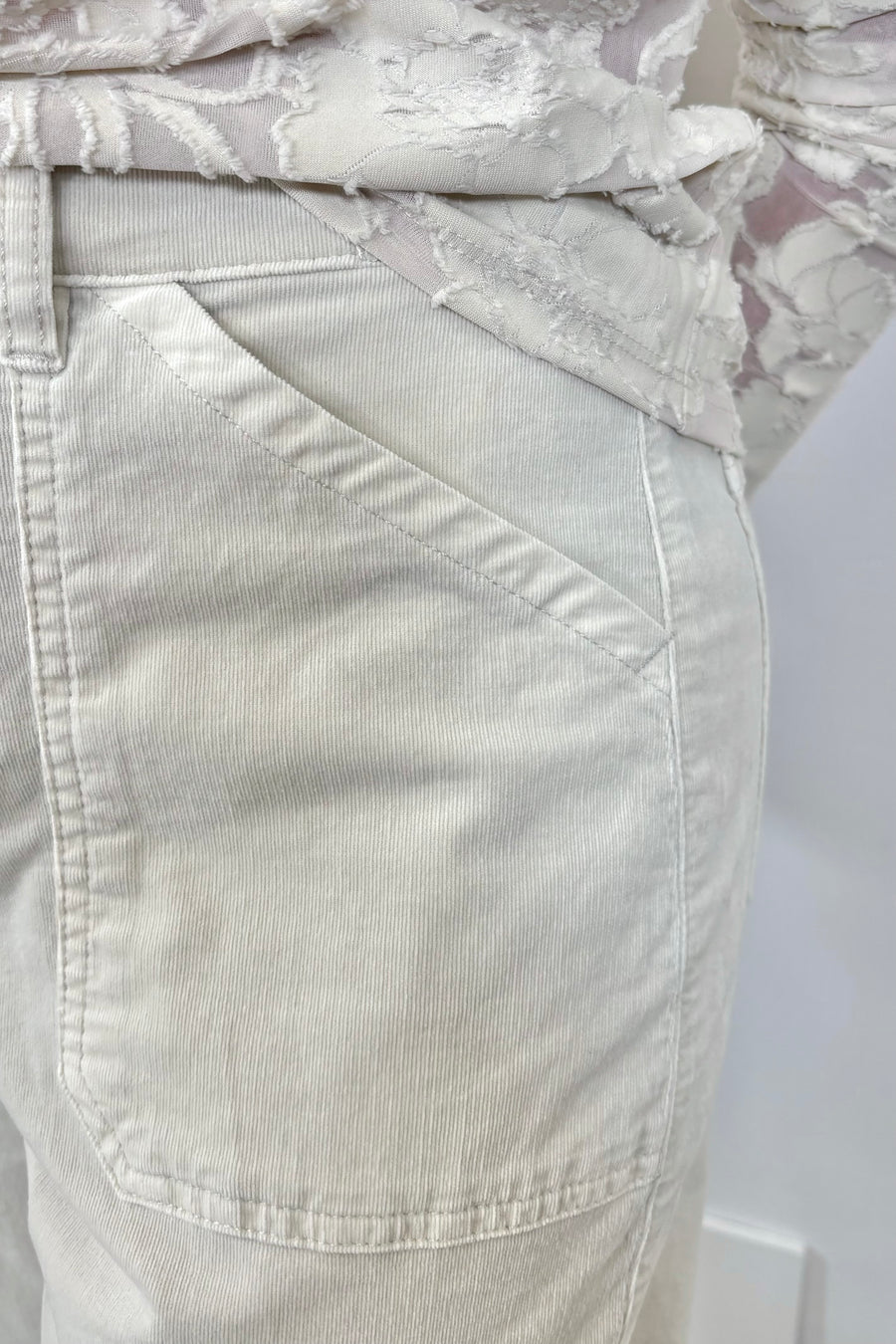 Close up view of a person wearing oat-coloured corduroy pants and white sneakers on a plain background