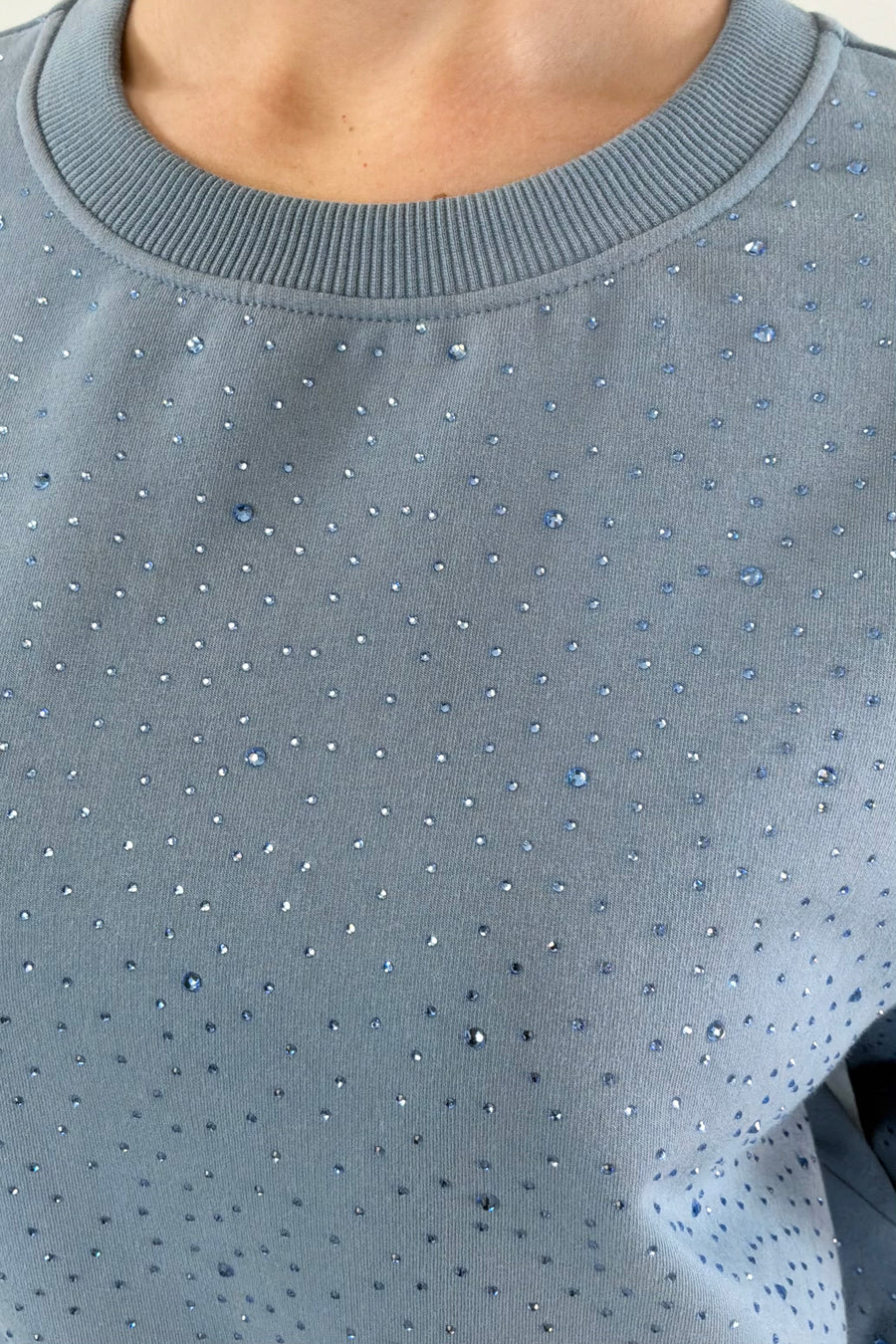Close up of Woman wearing blue pullover with rhinestone details all over