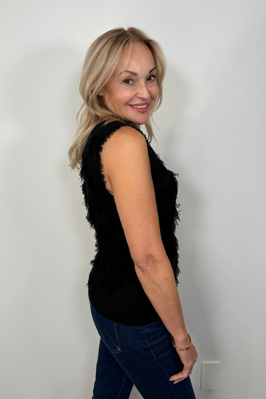 Side view a woman wearing a black tank top with fine gauge fringes 