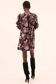 Woman wearing a floral dress with long sleeves and black knee-high boots on a light pink background