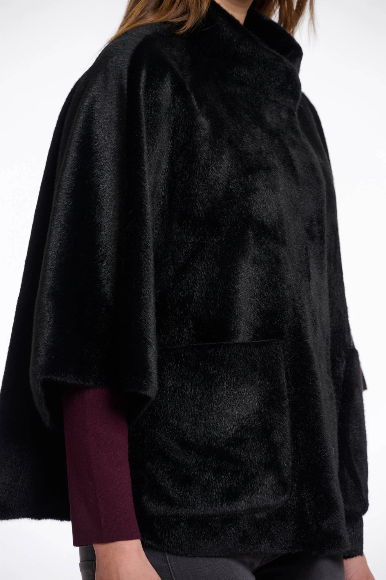 Close-up view of a woman wearing a black fur cape over a dark outfit on a white background