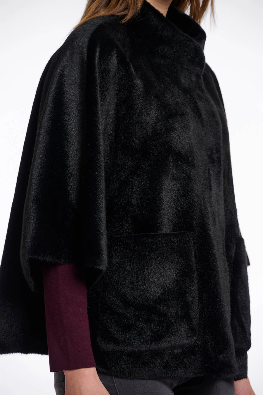 Close-up view of a woman wearing a black fur cape over a dark outfit on a white background