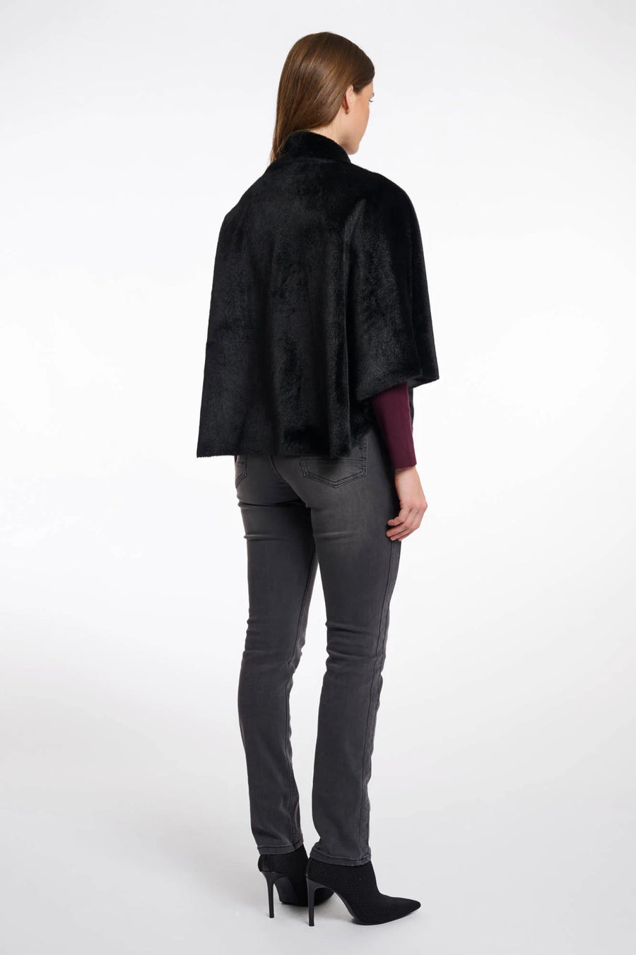 Back view of a woman wearing a black fur cape over a dark outfit on a white background