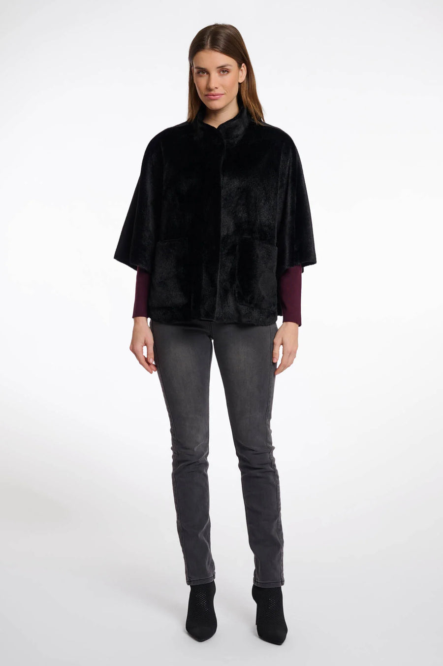 Full body view of a woman wearing a black fur cape over a dark outfit on a white background