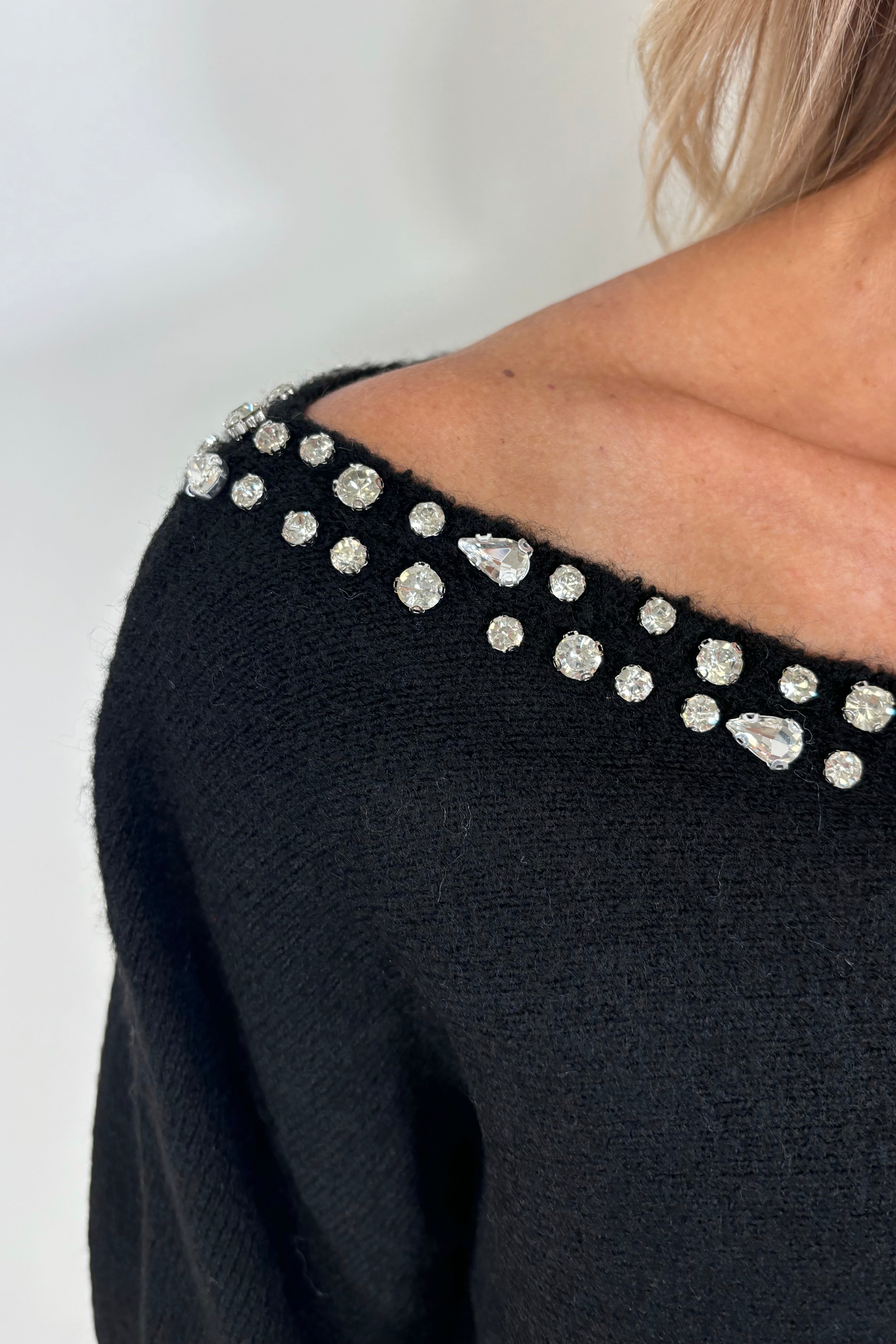 zoom in view of woman wearing a black sweater with rhinestones in the neckline