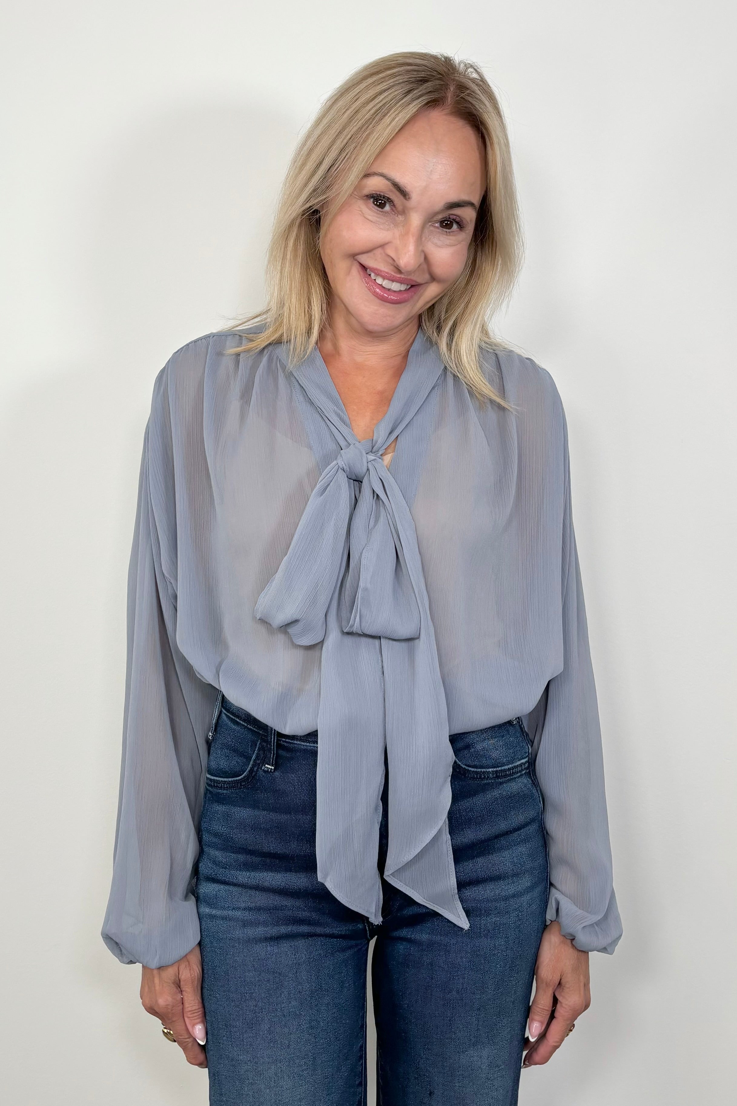 Front view of woman wearing a thin blue blouse with a bow and tucked in
