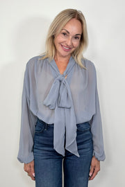 Front view of woman wearing a thin blue blouse with a bow and tucked in
