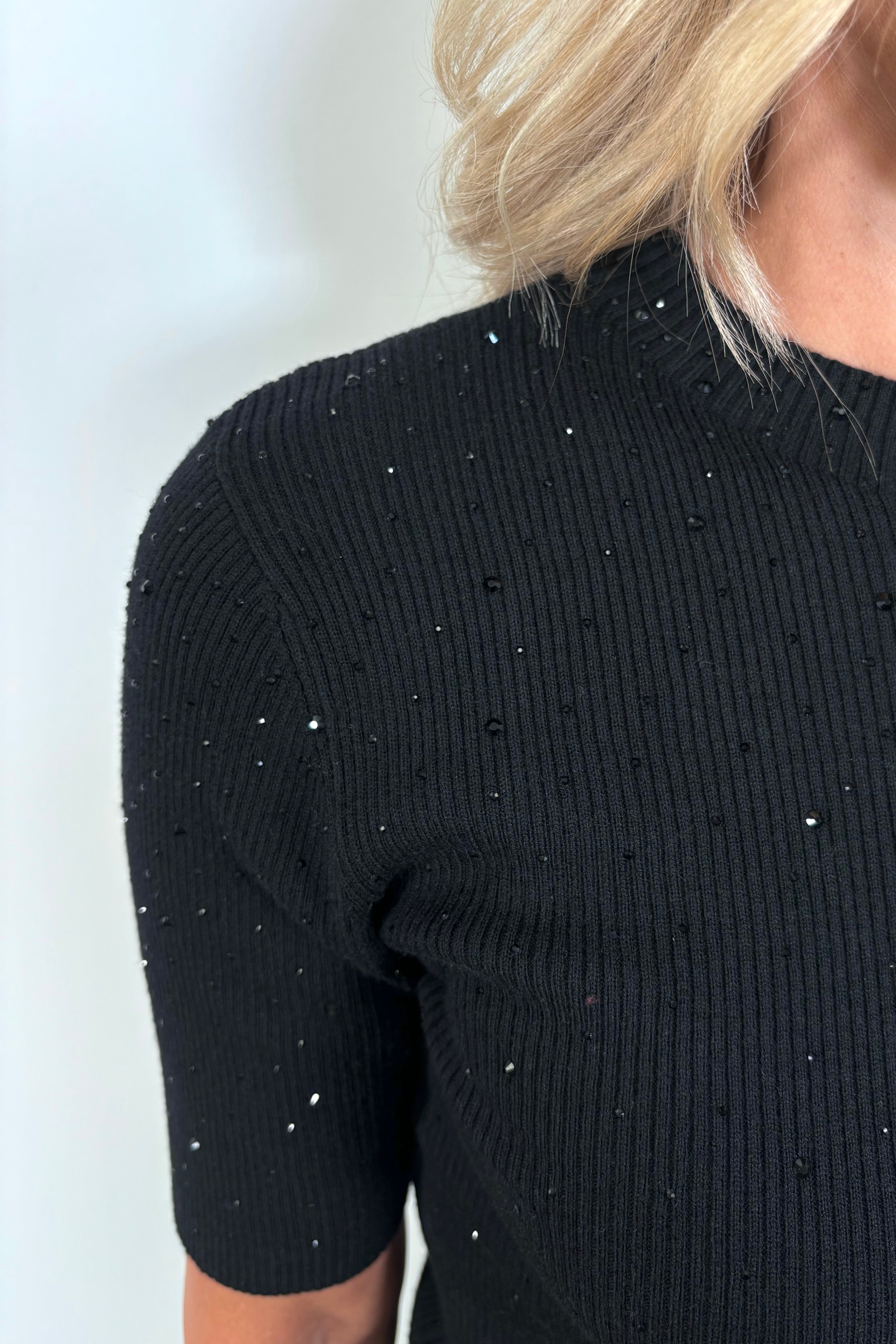 Close up of the shoulder of a woman wearing a black ribbed tee with crystal embellishments 