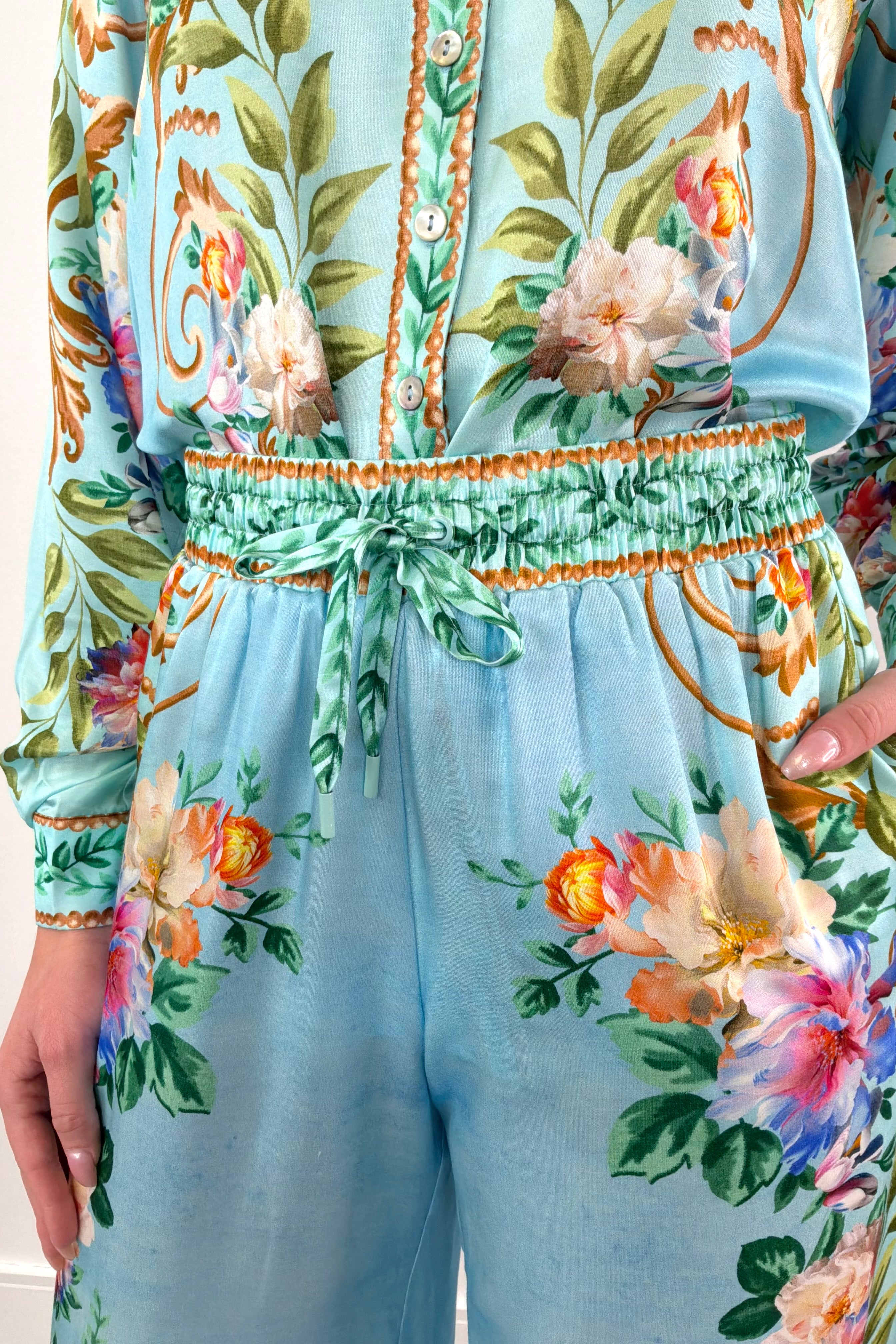 Close up of A woman wearing silk/viscose flowy pants in light blue with a floral pattern