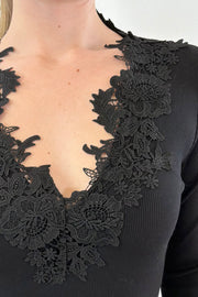 Close up of woman wearing a black ribbed top with lace details along the neckline