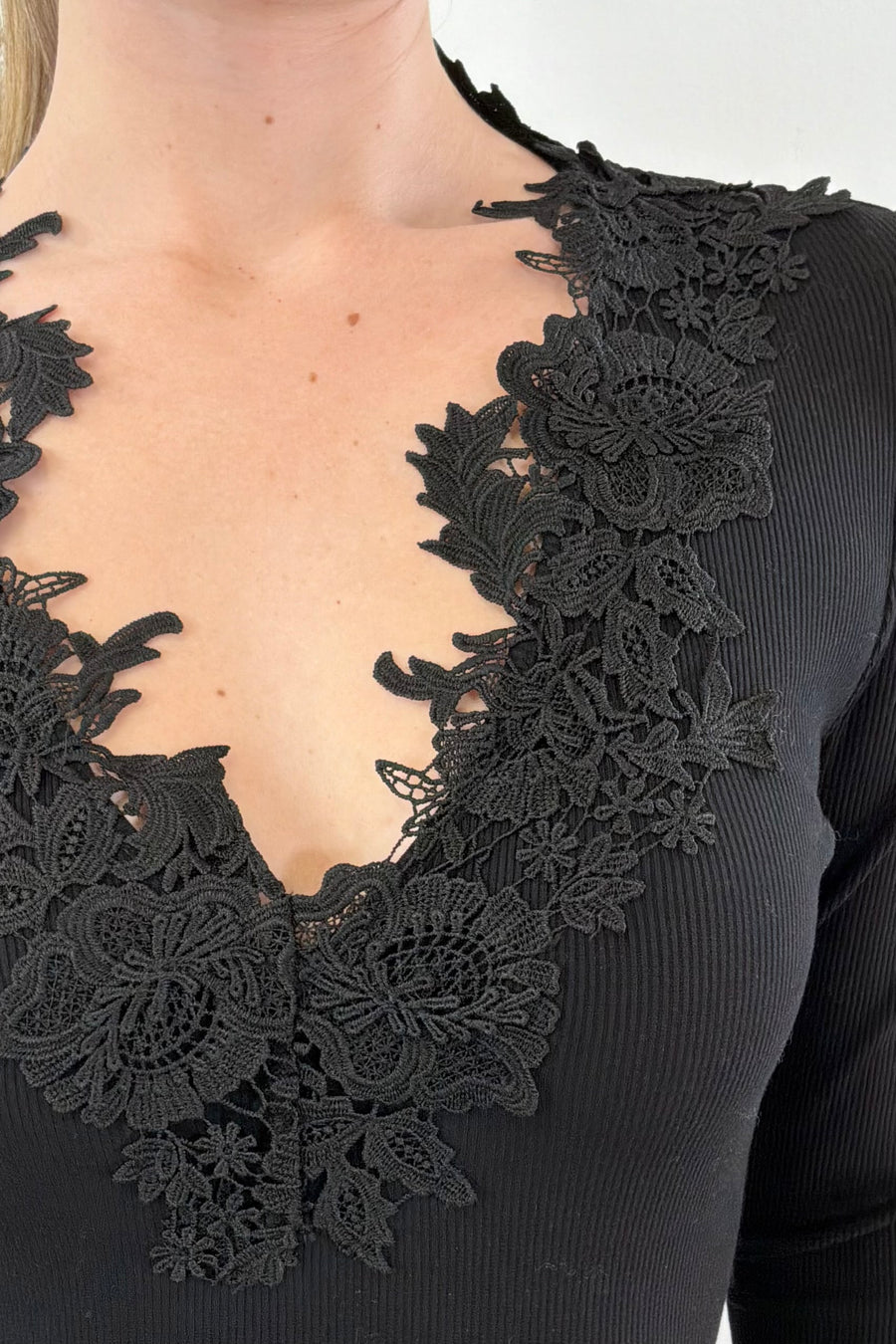 Close up of woman wearing a black ribbed top with lace details along the neckline