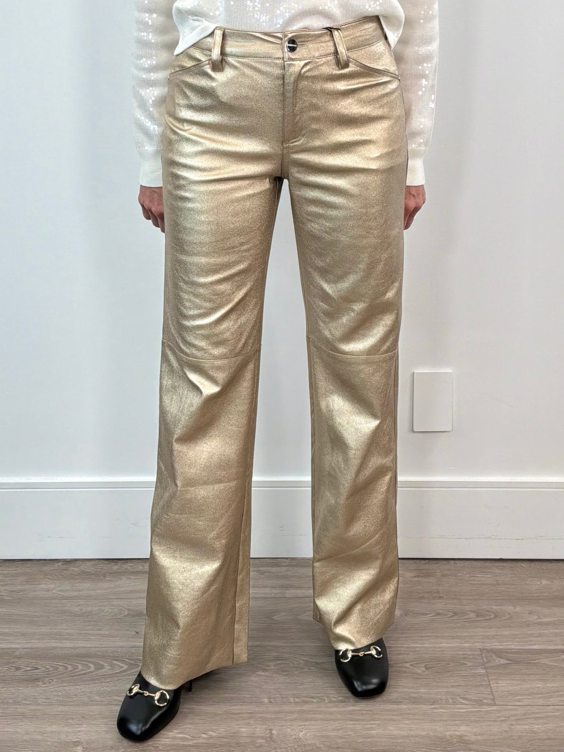 Person wearing gold metallic pants against a white wall.