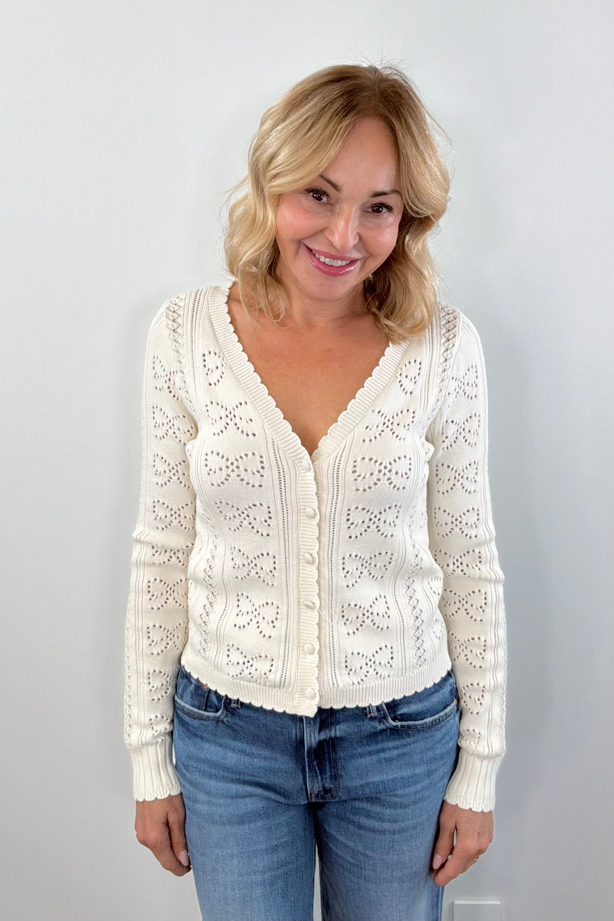 Woman wearing a cream cardigan with buttons on the front, scalloped trim and openwork detailing, front view