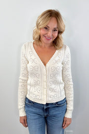 Woman wearing a cream cardigan with buttons on the front, scalloped trim and openwork detailing, front view