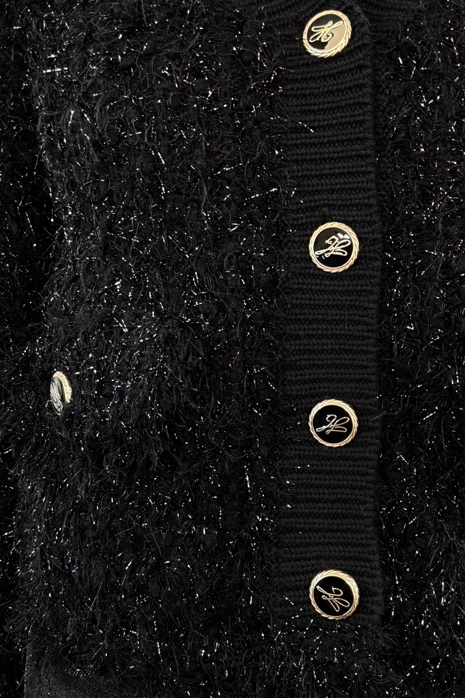 Close-up of a black textured cardigan with gold buttons on a black background
