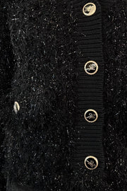 Close-up of a black textured cardigan with gold buttons on a black background