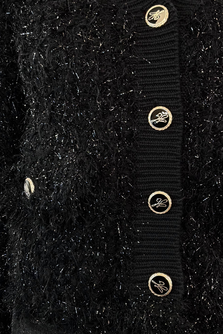 Close-up of a black textured cardigan with gold buttons on a black background