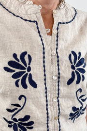 Woman wearing a cream sleeveless cropped top with blue embroidered detailing, detail view