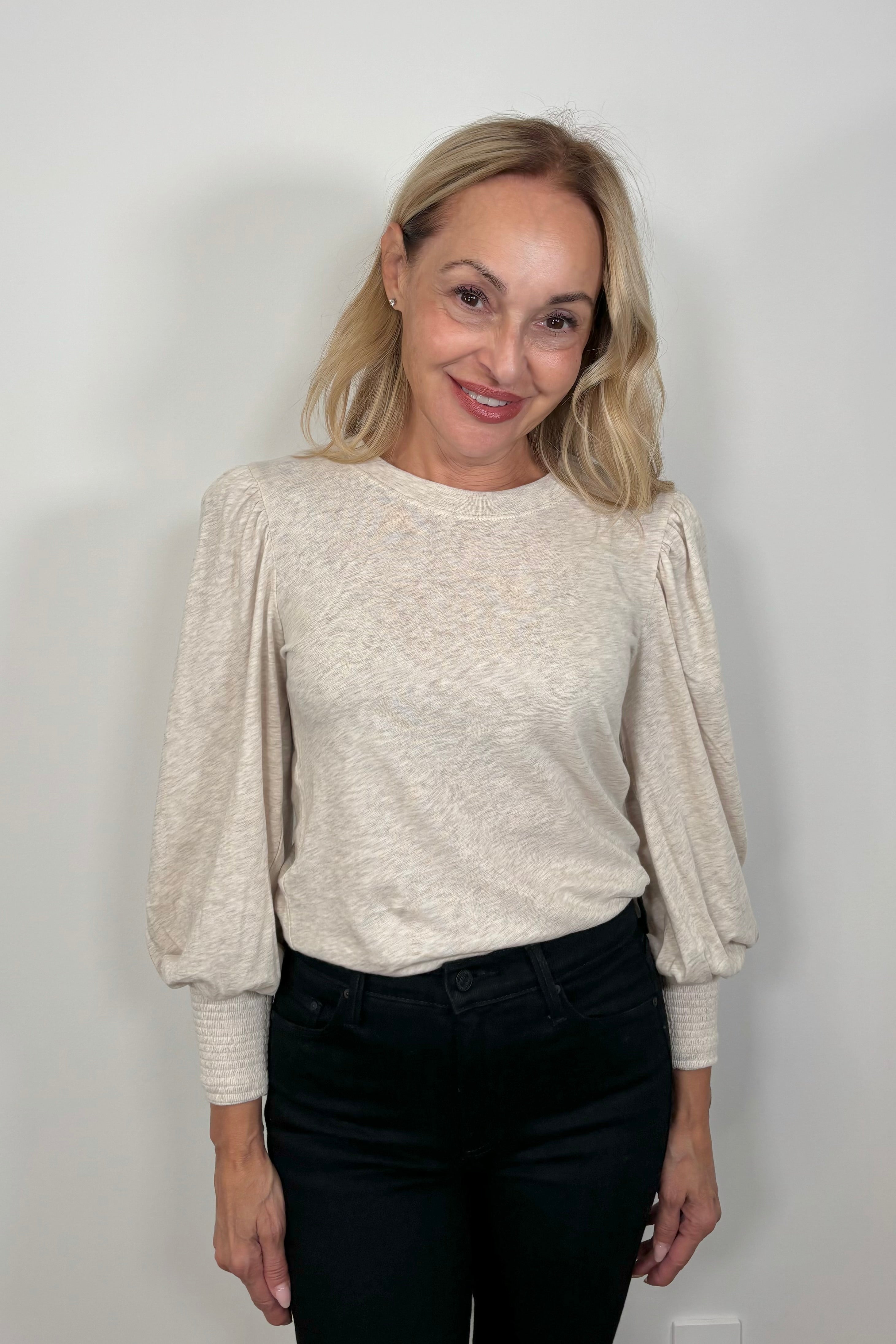 Woman wearing a beige long-sleeve top and blue jeans against a plain background