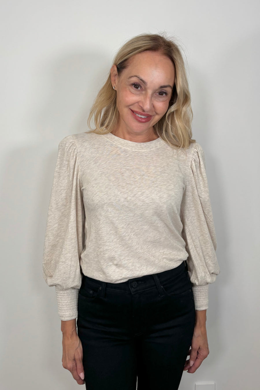 Woman wearing a beige long-sleeve top and blue jeans against a plain background