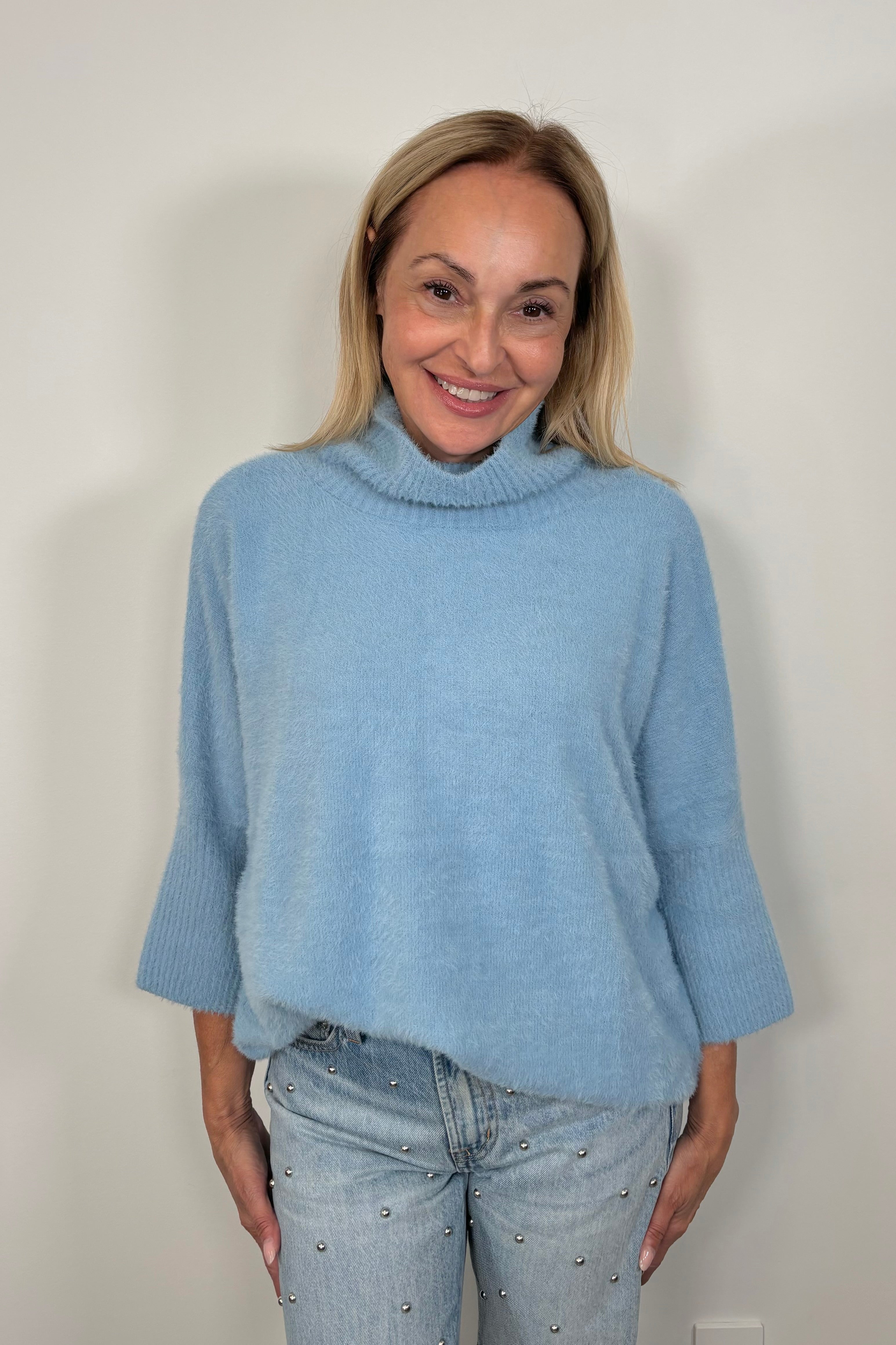 Front view of woman wearing a blue mock neck 3/4 sleeve sweater top