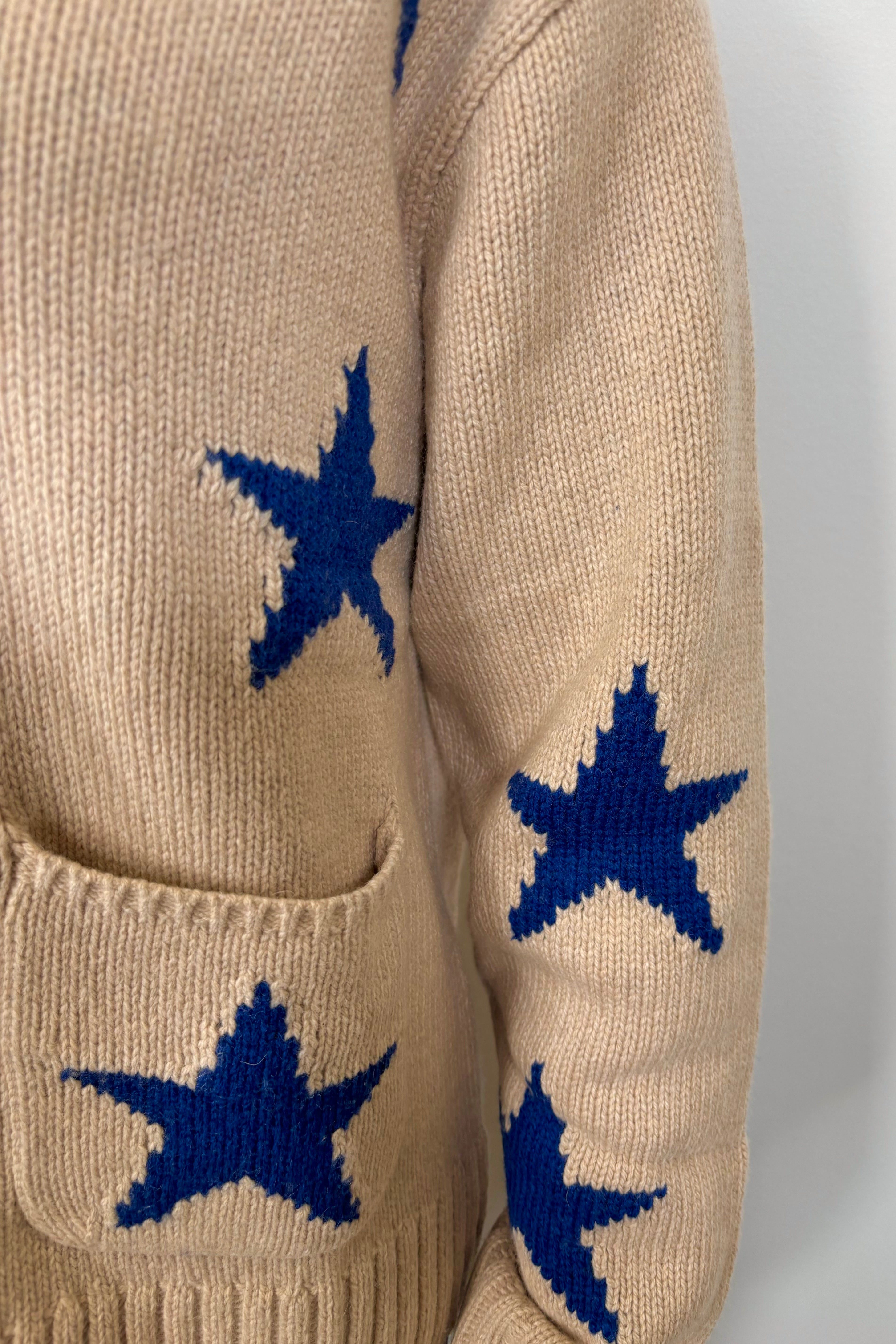 Close-up of a beige zip-up sweater with blue star patterns and front pockets