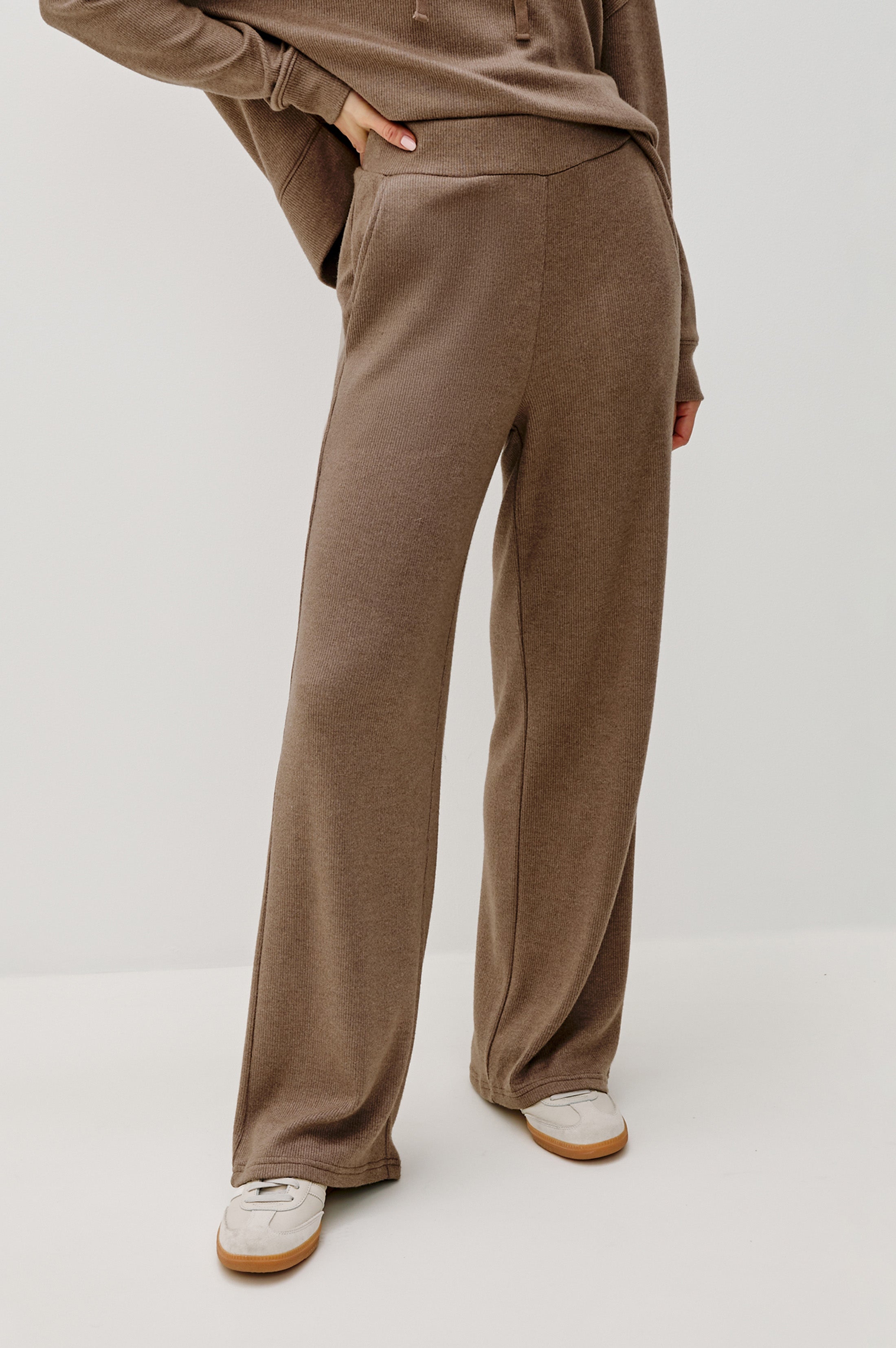 front view of a person wearing brown pants on a white background 