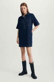 Woman wearing a dark blue denim dress with black boots on a light gray background