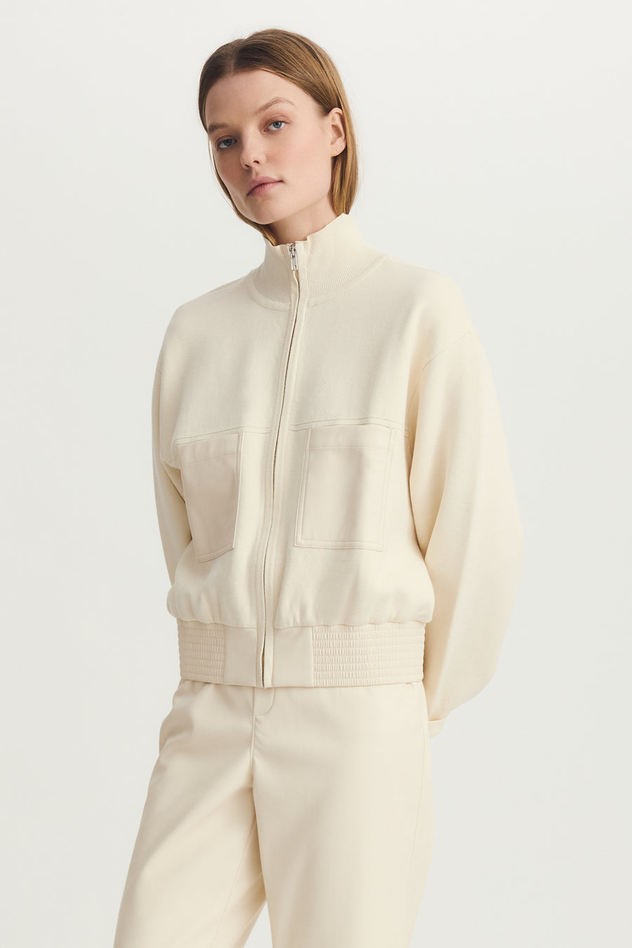 Woman wearing a cream mix media bomber jacket with front pockets