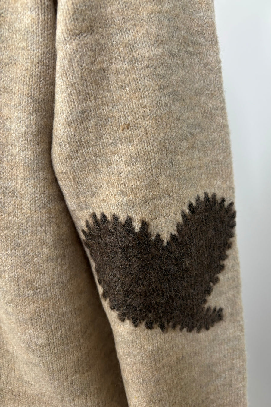 zoom in view of the heart detail on the elbow of a beige cardigan