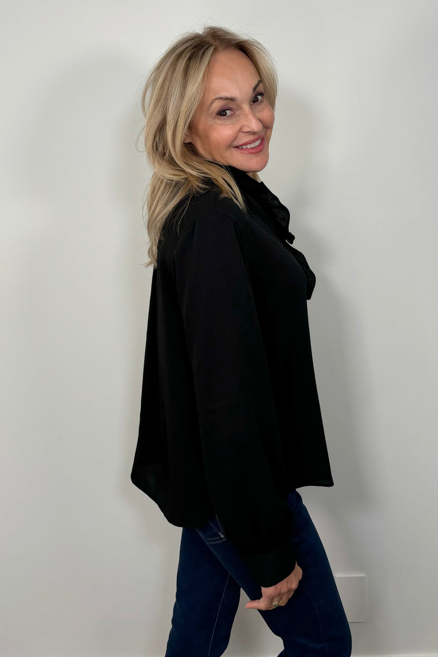 Side view of a woman wearing a black blouse with ruffles and blue jeans 