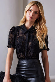 Woman wearing a black lace blouse and leather pants against a plain background