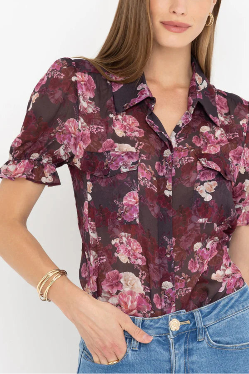 Woman wearing a black and pink floral blouse with a plain background