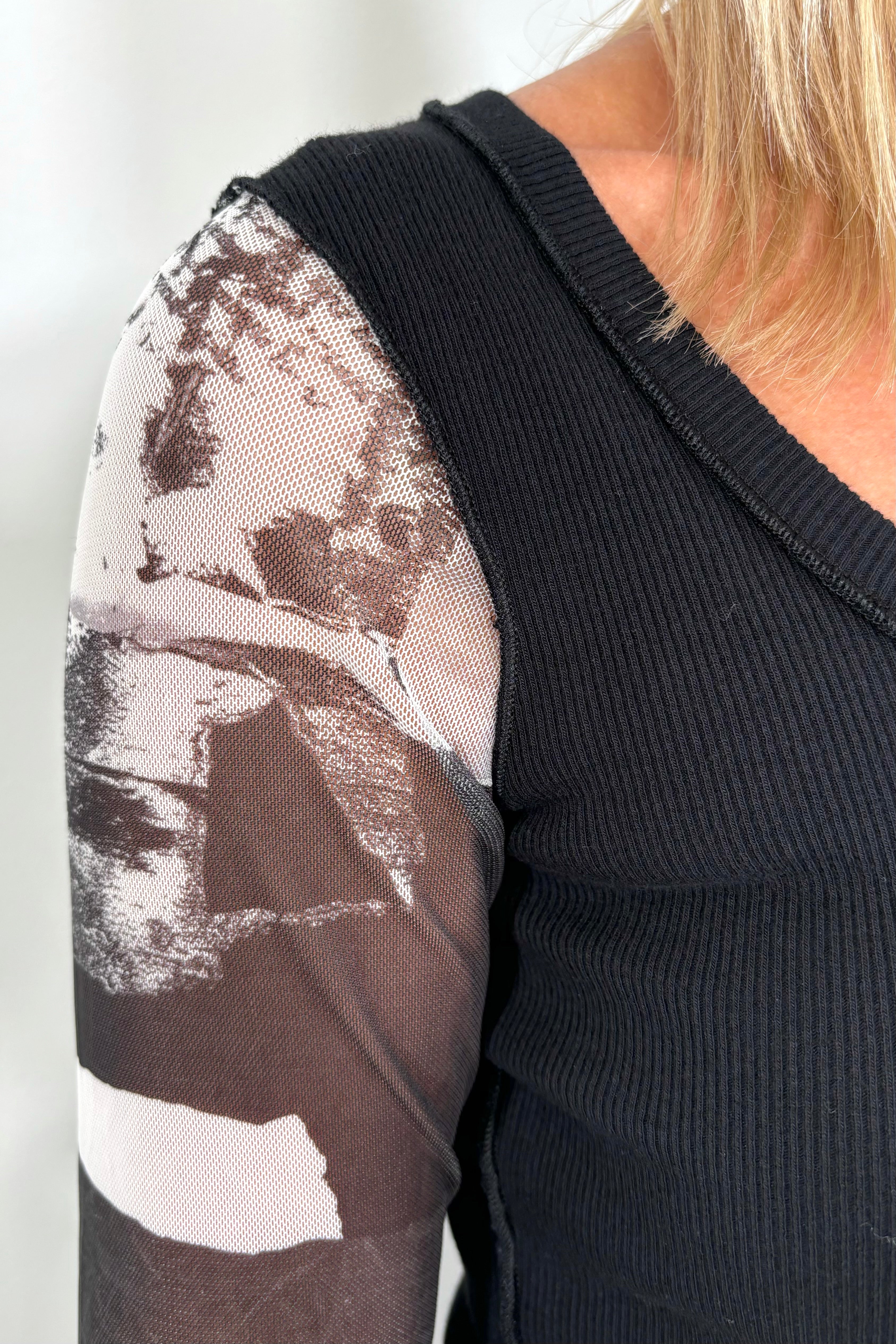 Front view zoom in shoulder of woman wearing a black torso mesh-long sleeve top with prints on the sleeves
