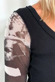 Front view zoom in shoulder of woman wearing a black torso mesh-long sleeve top with prints on the sleeves