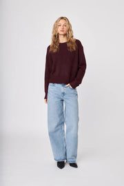 Full body front view of woman wearing a wine coloured crew-neck sweater and blue jeans