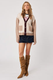Front view of woman wearing a colour block beige and burgundy cardigan with pockets with a denim mini skirt and tall brown boots