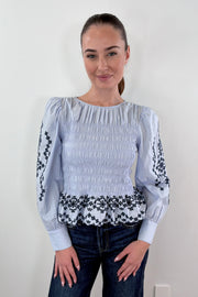 Woman wearing light blue smocked blouse with black detail
