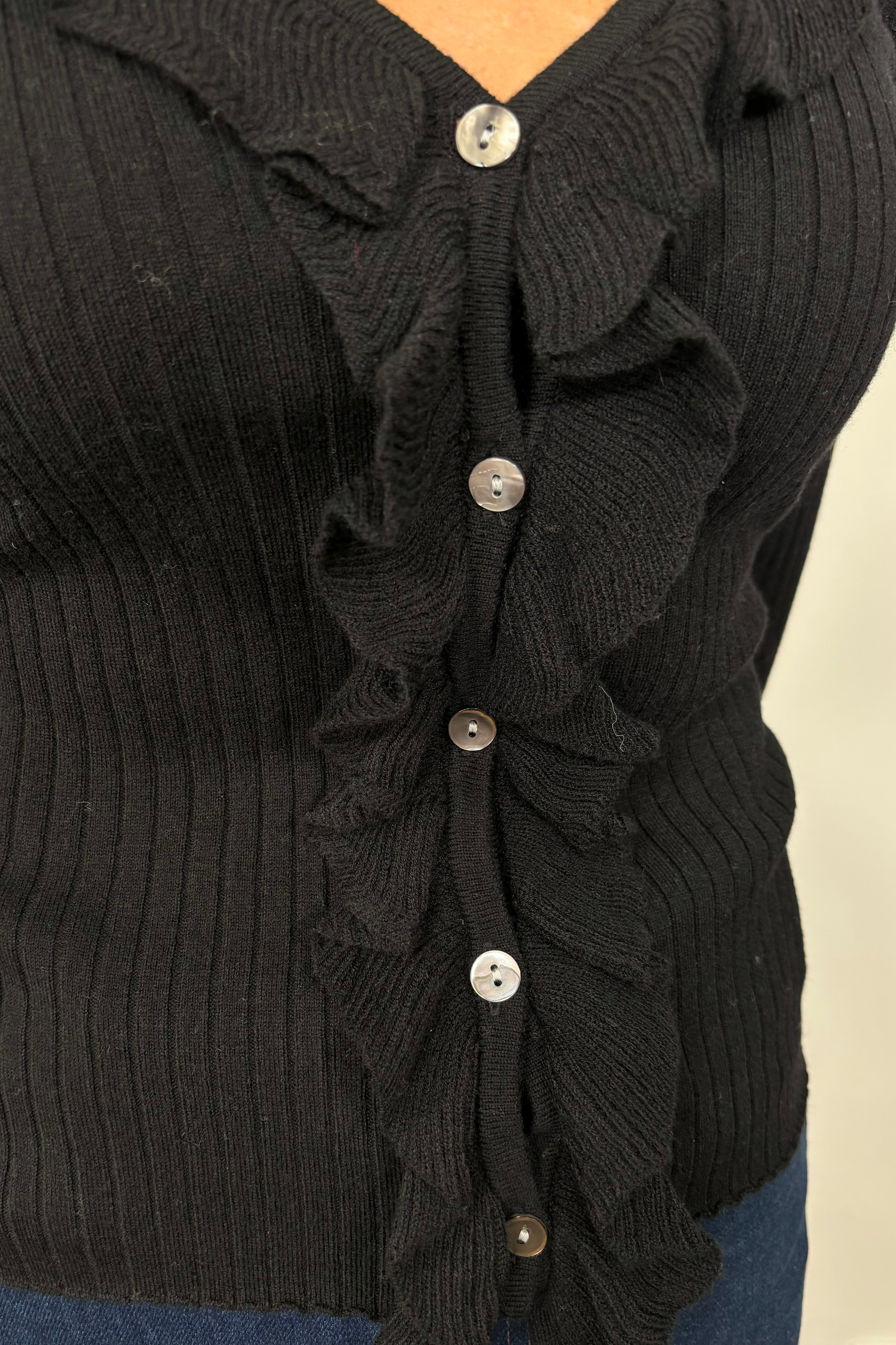 Zoom in of woman wearing a black v-neck with ruffles long sleeve ribbed top.
