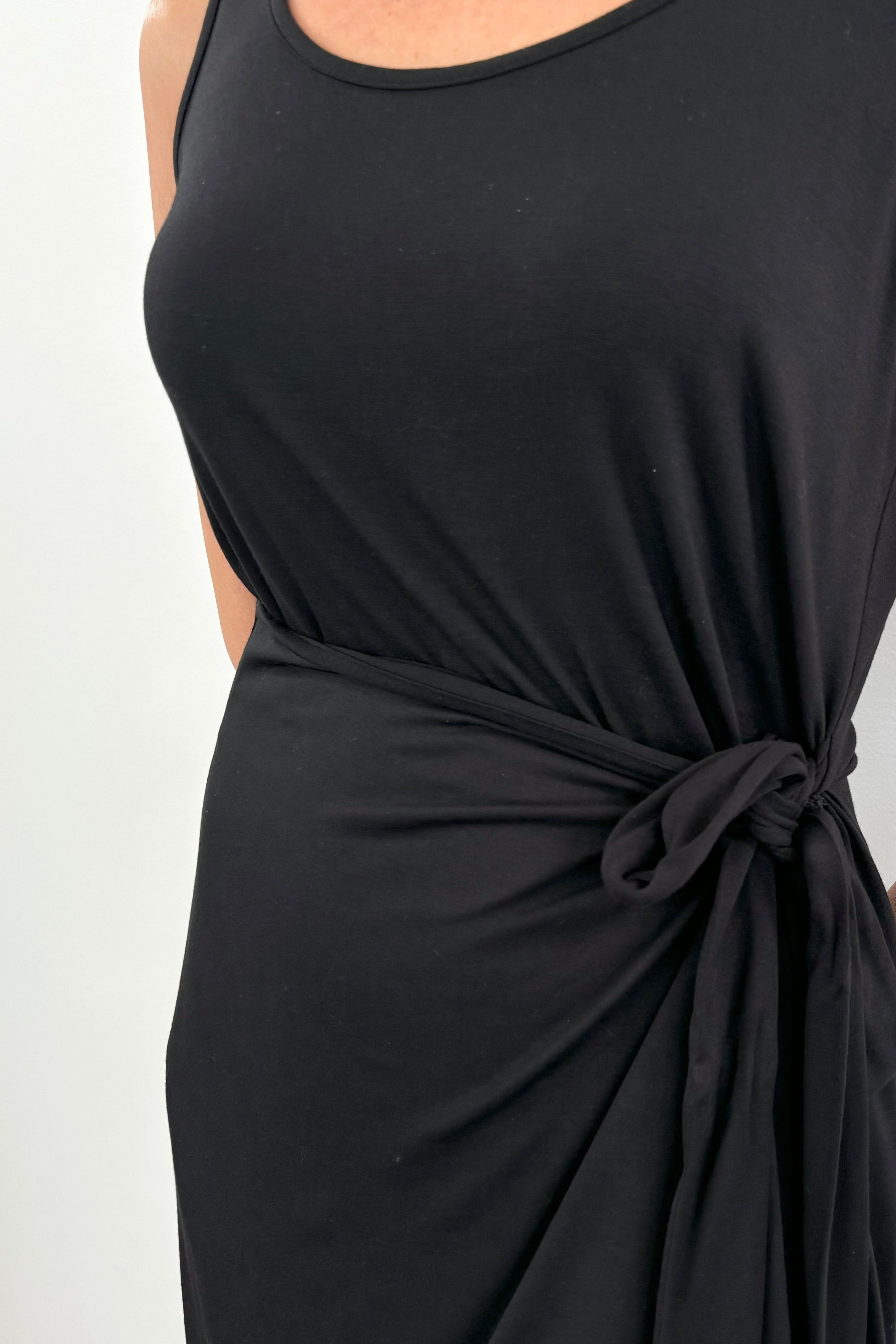 Close up of woman wearing a black midi dress with bow detailing n the side